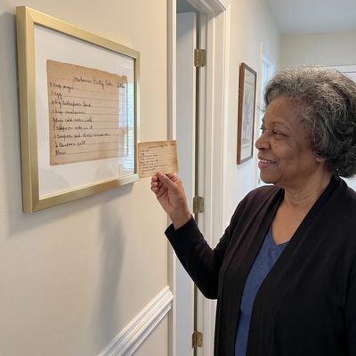 A woman holds the original Molasses Party Cake card beside its framed print in a gold frame.